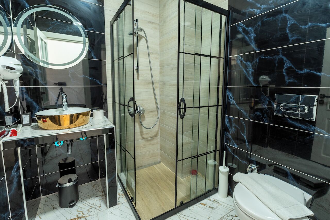 A modern bathroom with a glass-enclosed shower, a round sink with a gold basin, and a toilet.