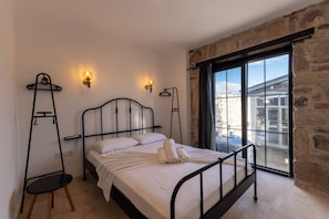 Una cama con estructura metálica, ropa de cama blanca y dos lámparas fijadas a la pared.