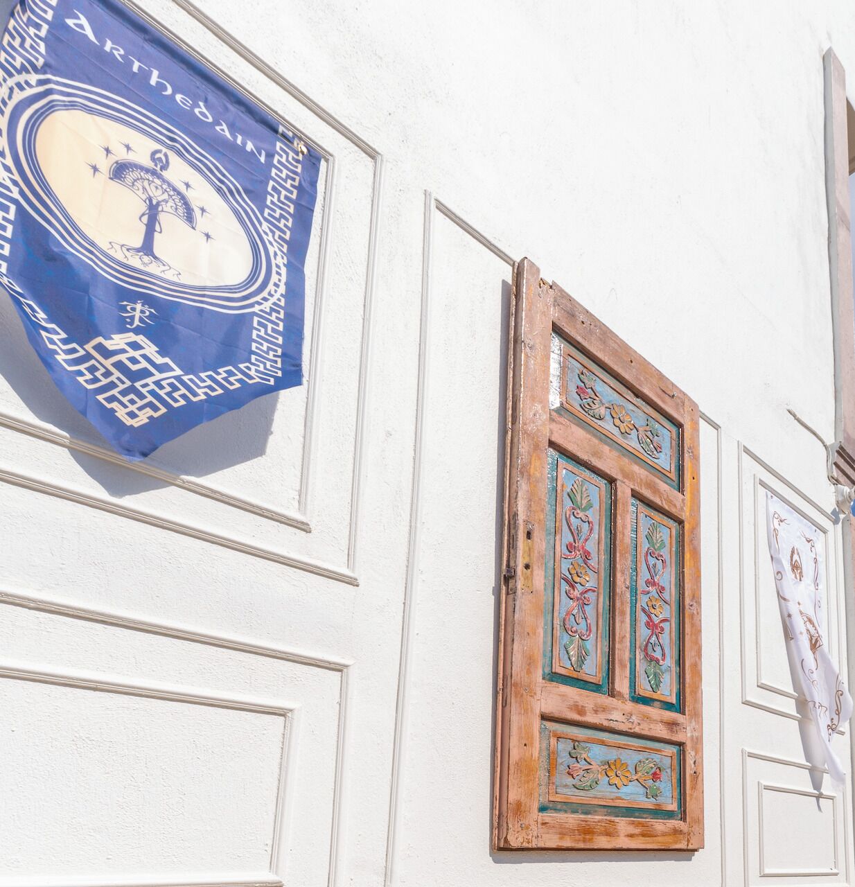 A building facade with a blue banner featuring a tree and stars, a wooden door with floral designs, and a white wall with decorative moldings.
