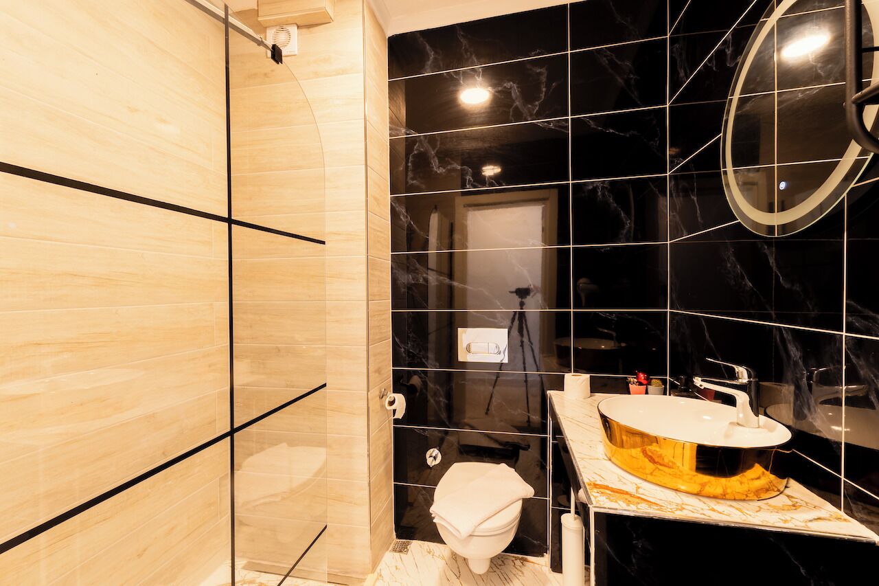 Un baño moderno con ducha envuelta en vidrio, pared con azulejos de mármol y tocador con un espejo grande.