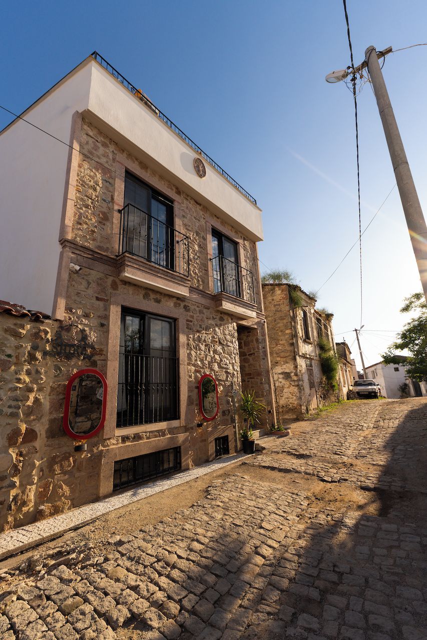 A two-story stone building with a balcony, a cobblestone street, and a utility pole.