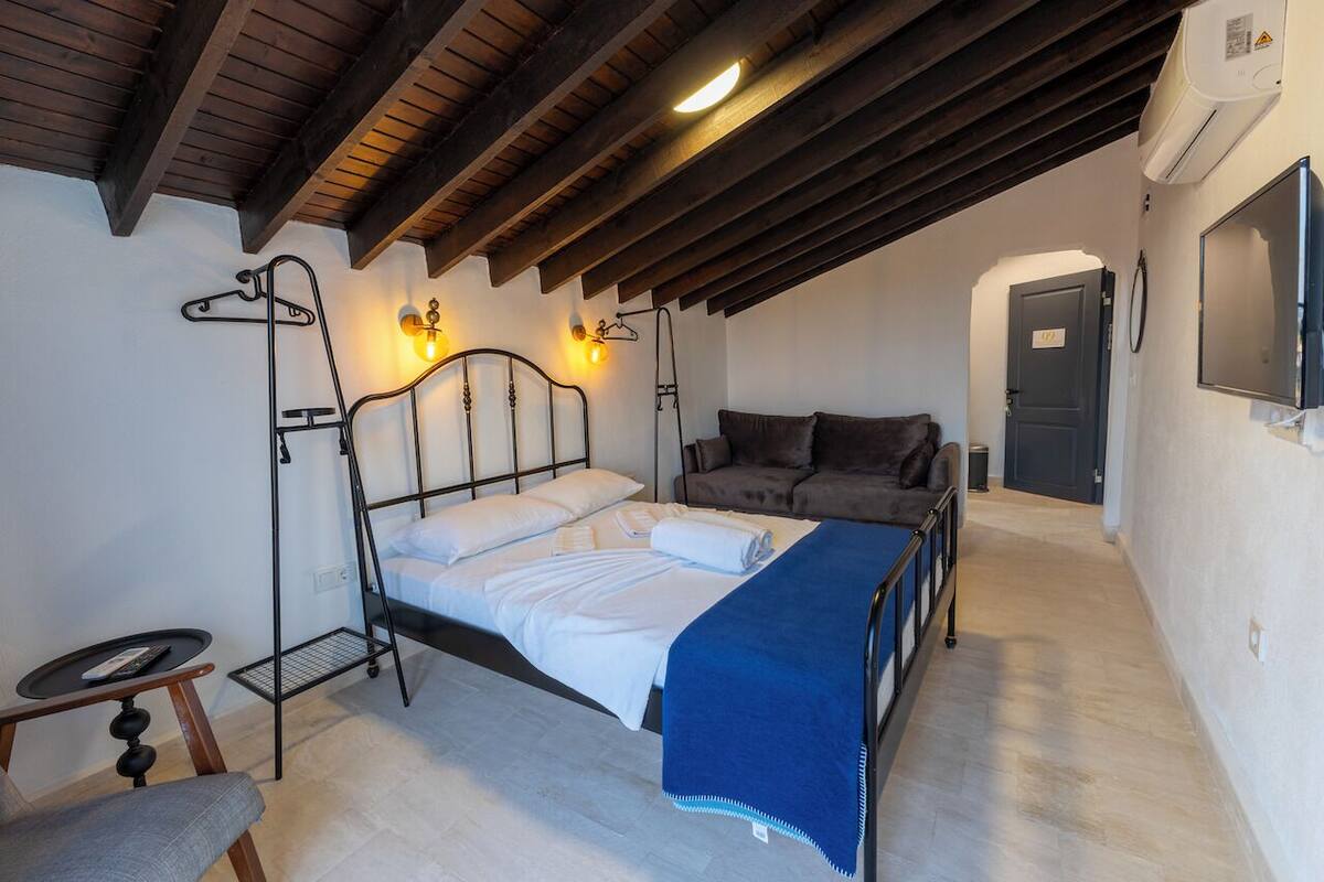Un dormitorio con cama, sofá, una mesita y televisor montado en la pared.