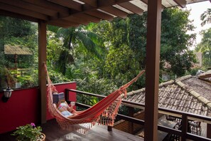 A hammock on a balcony with a view of lush greenery and traditional architecture.