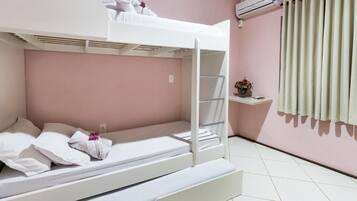 Dormitorio con literas, colchón blanco, almohadas y una pequeña estantería con flores.