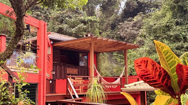Un edificio rojo con terraza de madera y hamaca.