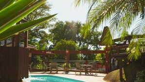 Un área de piscina con sillones de descanso, una pérgola de madera y palmeras.