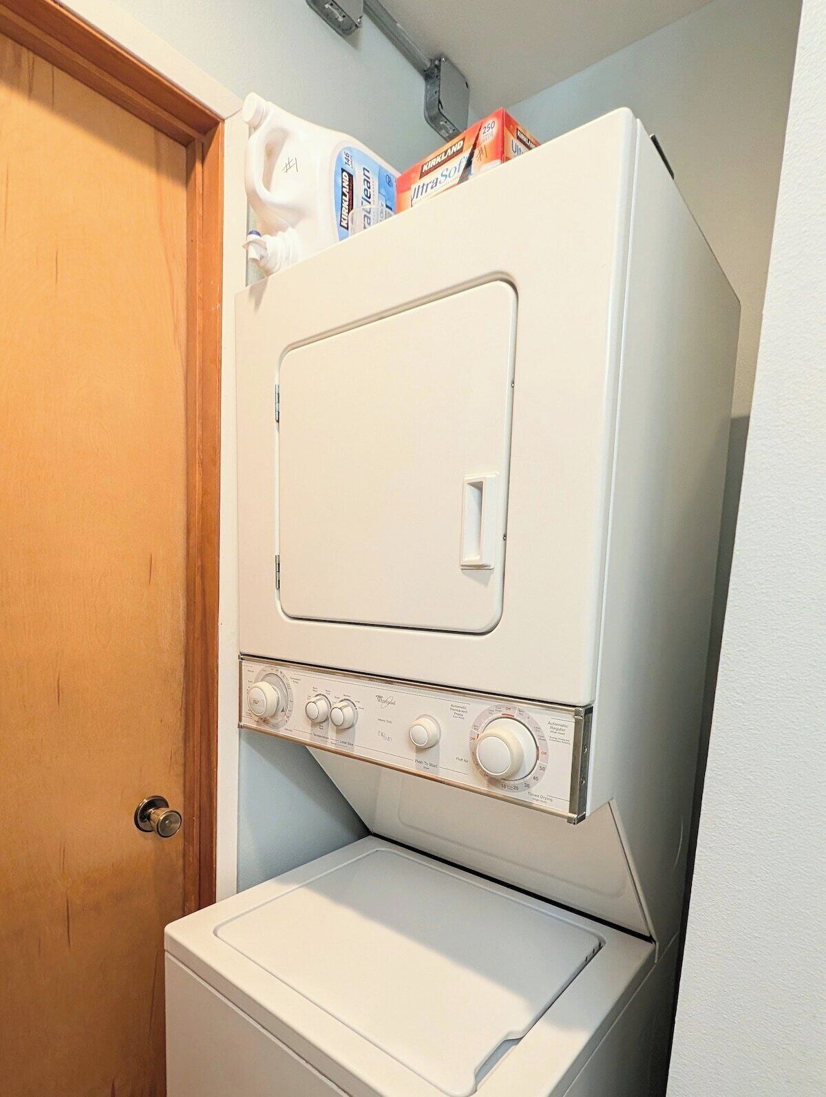 A compact washer and dryer unit with a control panel, located in a small laundry room with a wooden door.