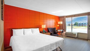 A hotel room with a large bed, a chair, a desk, and a large window.