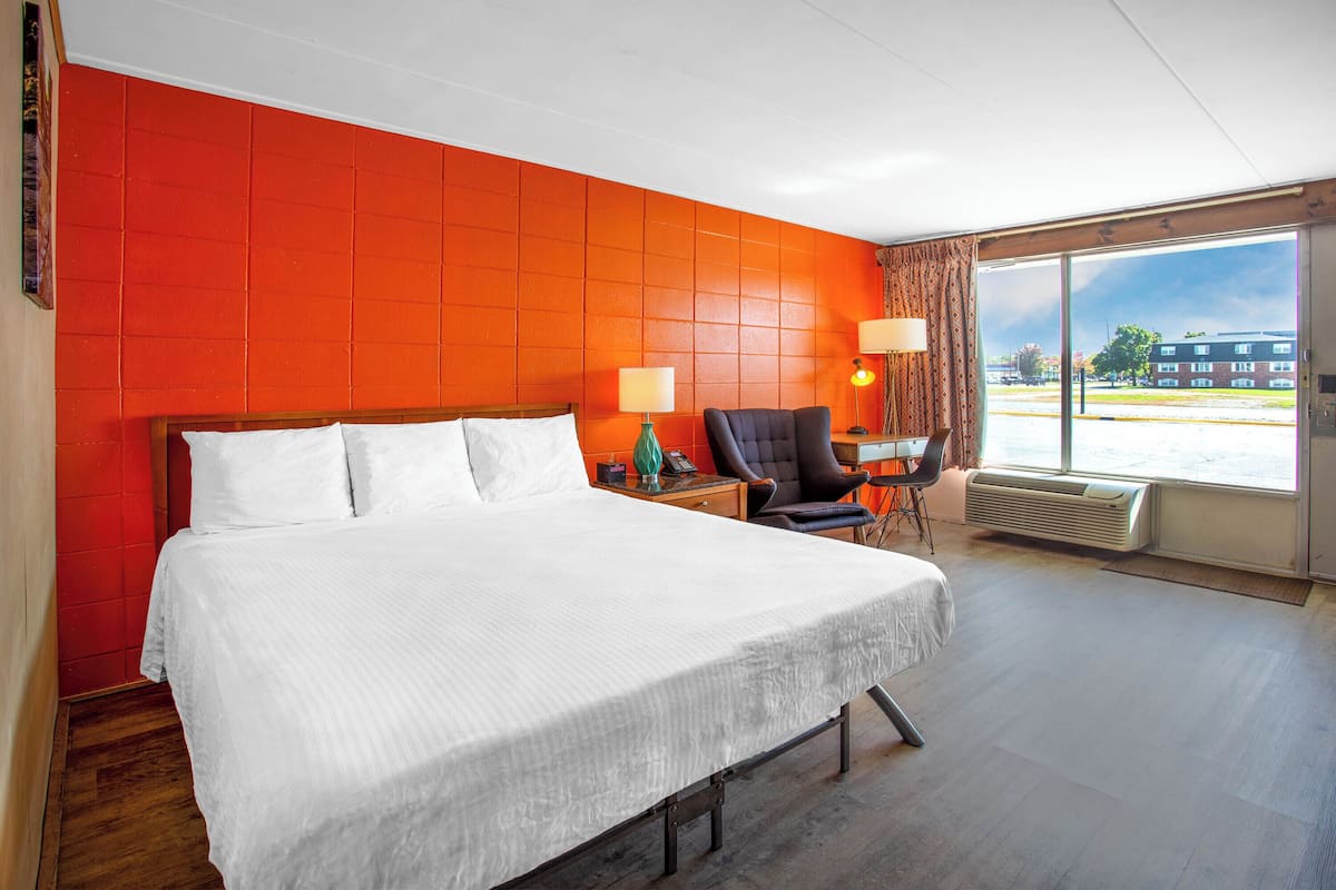 A hotel room with a large bed, a chair, a desk, and a large window.