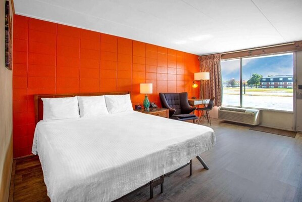 Ein Hotelzimmer mit einem großen Bett, einem Sessel, einem Tisch und einem Fenster mit Blick nach außen.