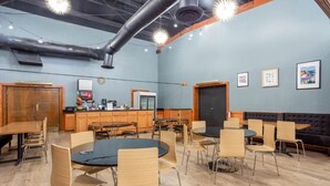 A conference room with round tables and chairs, a kitchenette, and a black sofa.