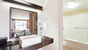 A bathroom with a white sink, dark countertop, mirror, and a shower area.