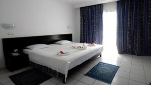 Ein Hotelzimmer mit einem großen Bett, einem Nachttisch, einem Schreibtisch und einem Fenster mit Vorhängen.