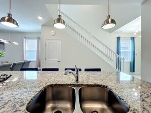A kitchen with granite countertops, stainless steel sink, pendant lights, and a staircase leading to another level. - Exquisite 7 beds Pool Home minutes from Disney World! (Davenport)