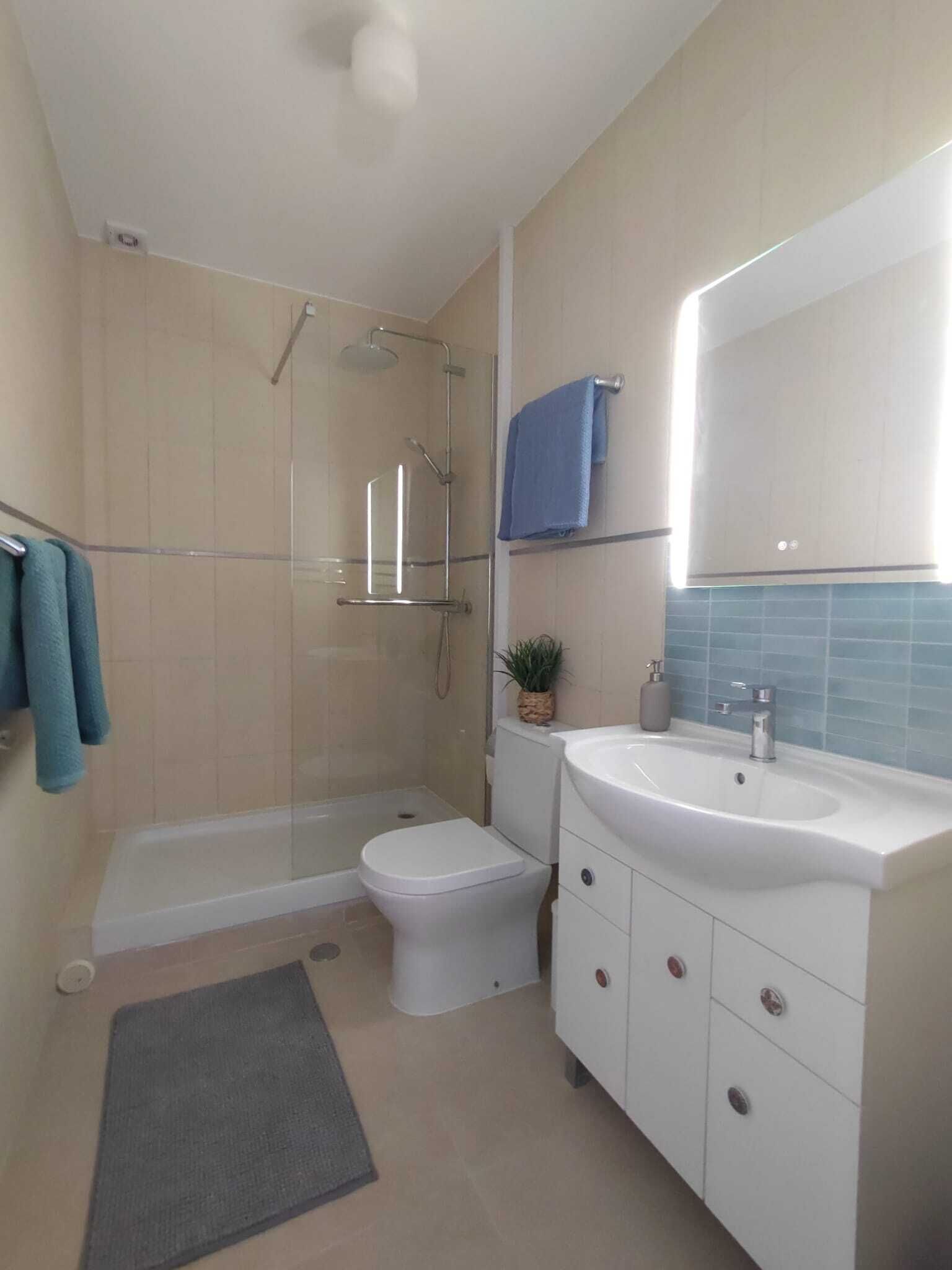A modern bathroom with a glass-enclosed shower, a white toilet, a sink with a mirror, and a blue towel rack.