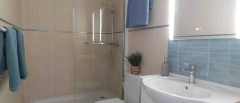 A modern bathroom with a glass-enclosed shower, a white toilet, a sink with a mirror, and a blue towel rack.