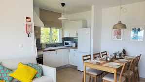 A compact kitchen with white cabinets, a microwave, and a sink. There's a dining table with chairs and a sofa with colorful cushions.