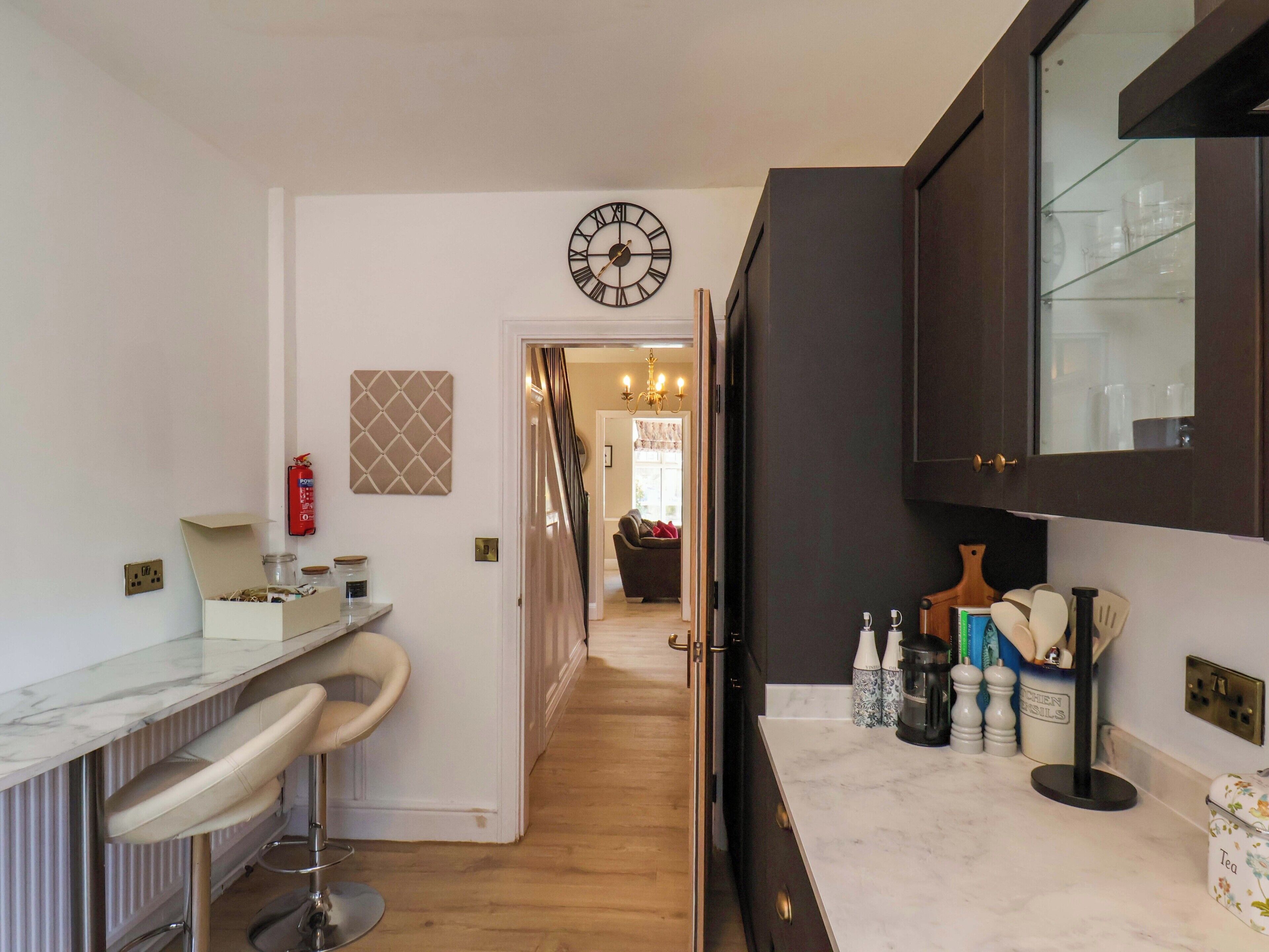 A kitchen with a marble countertop, a bar area with stools, a clock, and cabinets.