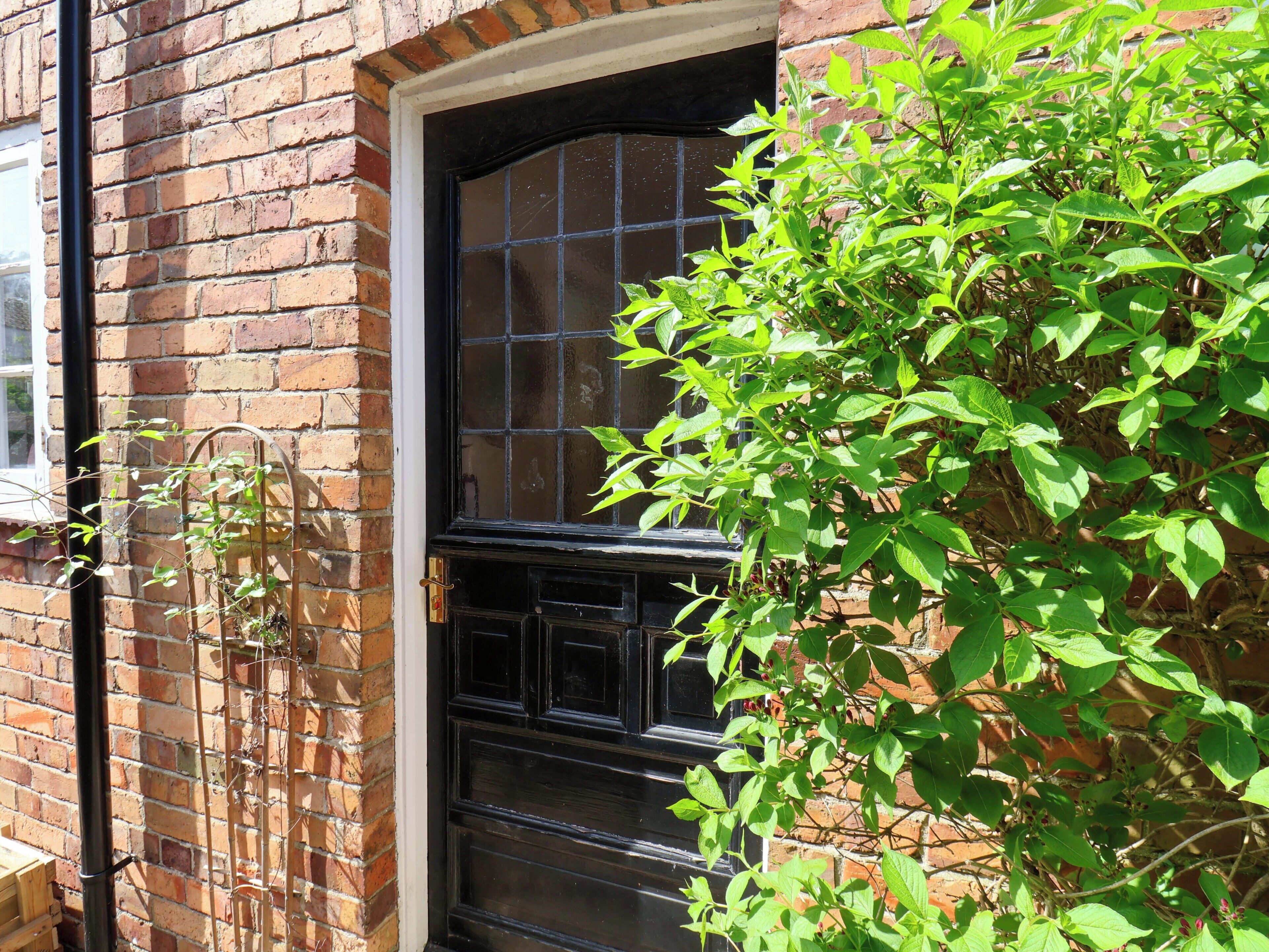 A brick building with a black door and window, a metal gate, and green foliage.