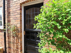 A brick building with a black door and window, a metal gate, and green foliage. - 16 High Street (Scarborough)