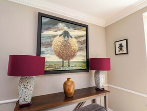 A framed artwork of a sheep on a wall, two lamps on a console table, and a vase.