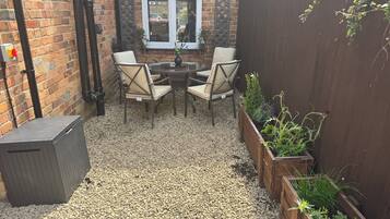 Un patio con una mesa, sillas, un muro de ladrillo, una ventana y una valla de madera.
