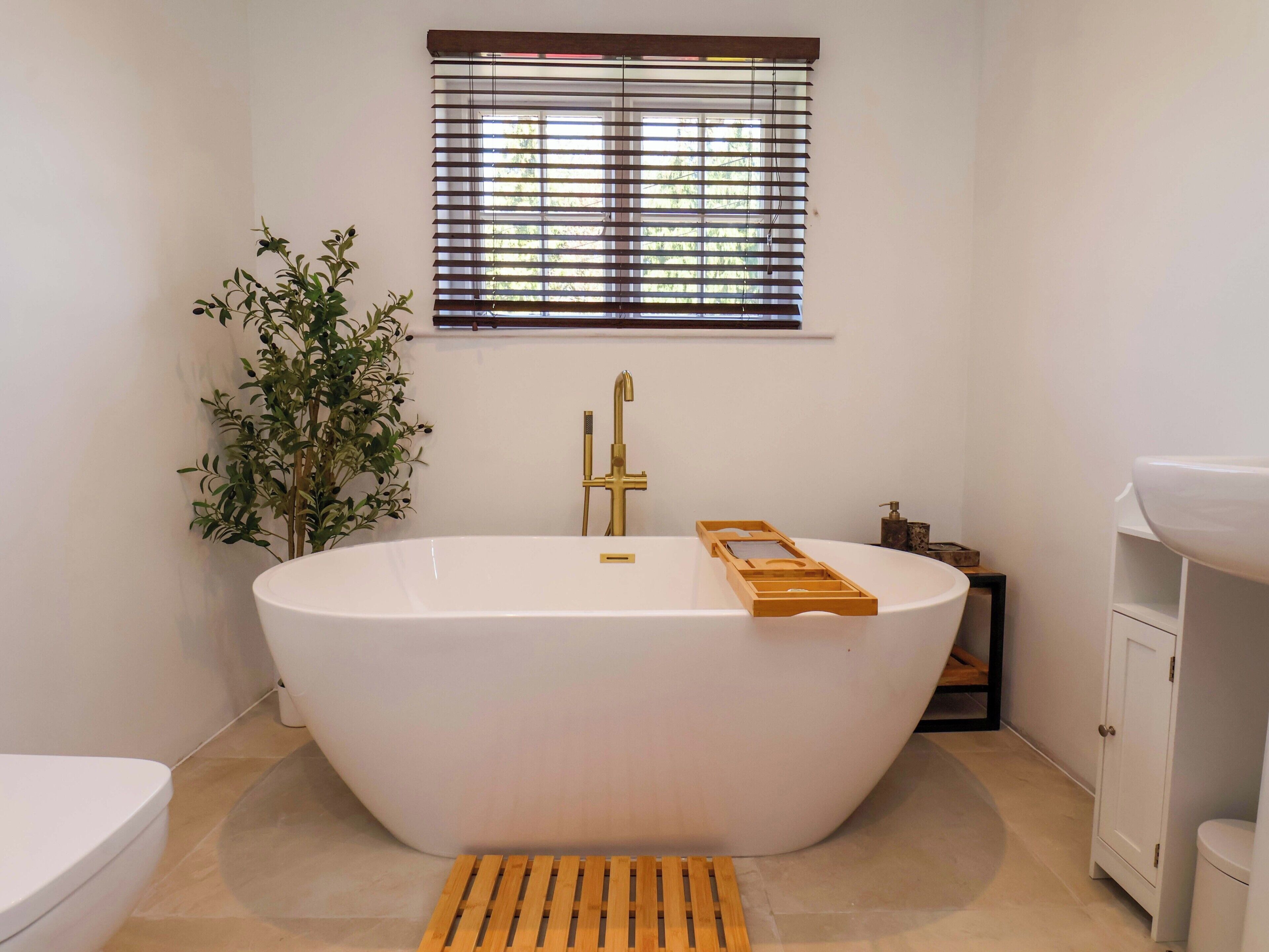 Une salle de bain avec une baignoire sur pieds, une fenêtre avec des stores, une plante en pot et un lavabo blanc.