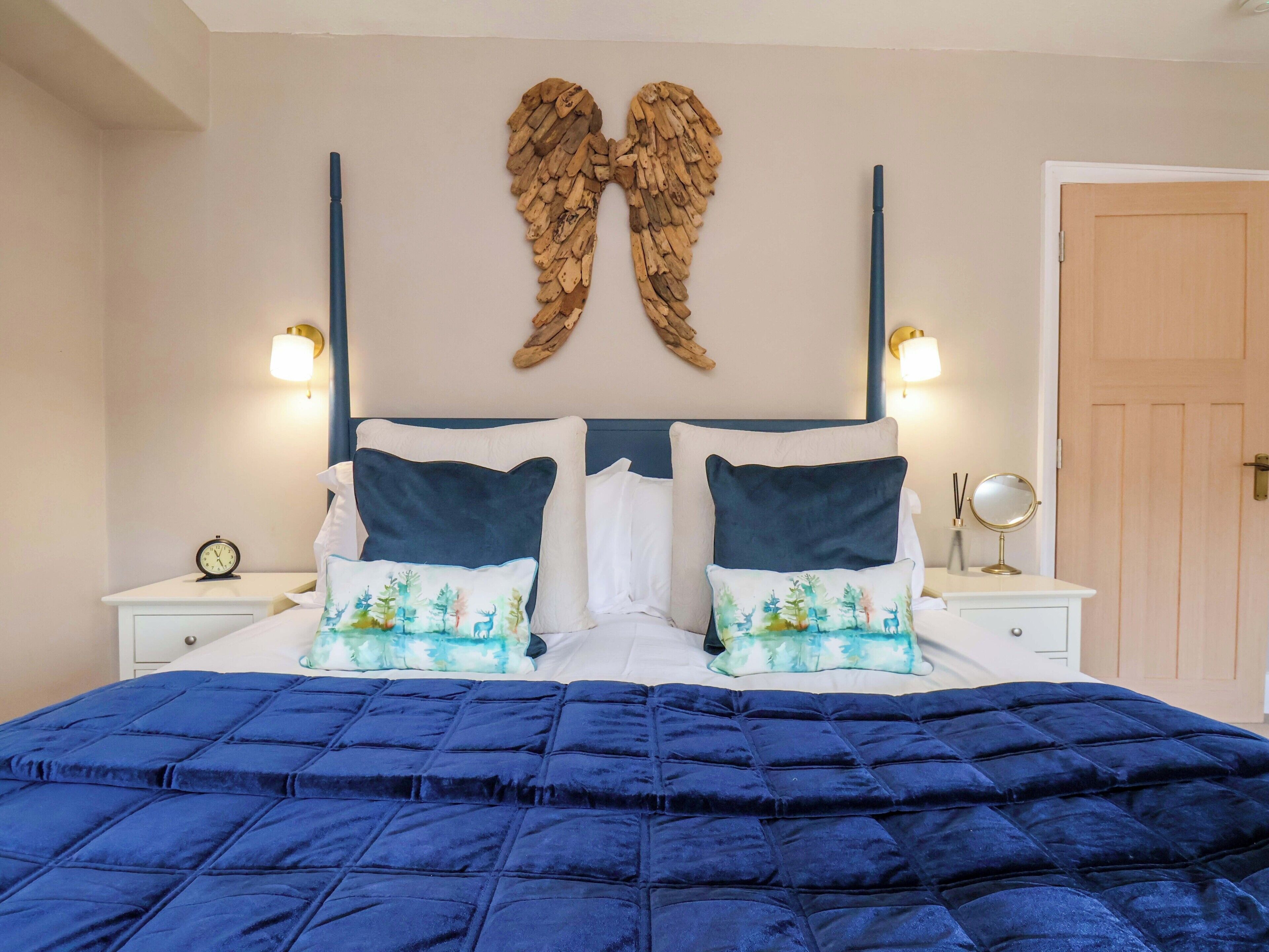 A bedroom with a bed, two nightstands, a wall-mounted mirror, a clock, and a door.
