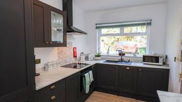 Una cocina moderna con muebles oscuros, estufa integrada, ventana con vistas y un microondas en la encimera.