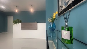 Una recepción con una planta, un florero con flores y una botella de perfume sobre una mesa de vidrio.
