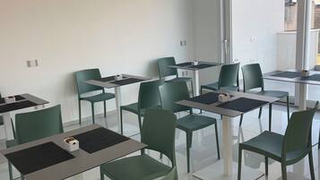 A modern, well-lit room with a large glass door leading outside, several tables with chairs, and a clean, minimalist design.