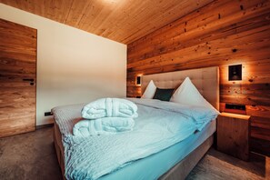 A bedroom with a wooden ceiling, a bed with a white duvet and pillows, and a nightstand with a lamp. - Forestum - Black Forest Luxury Apartments - Apartment Rothirsch with sauna (Sankt Blasien)