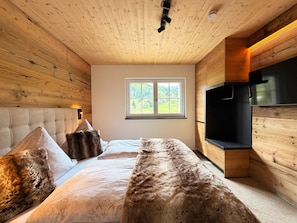 Ein Schlafzimmer mit einem großen Bett, Holzwänden, einem Fenster mit Blick und einem eingebauten Fernseher.