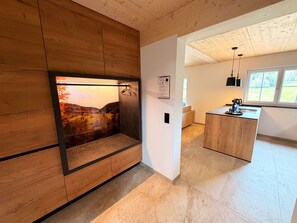 Een modern interieur met een wandmeubel van hout, een keukenhoek en uitzicht op een landschap door een raam.
