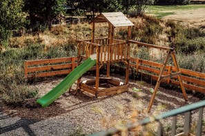 A wooden playground structure with a slide and climbing area, surrounded by grass and trees. - Forestum - Black Forest Luxury Apartments - Apartment Rothirsch with sauna (Sankt Blasien)