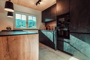 A modern kitchen with a wooden island, a large window, and built-in appliances. - Forestum - Black Forest Luxury Apartments - Apartment Rothirsch with sauna (Sankt Blasien)