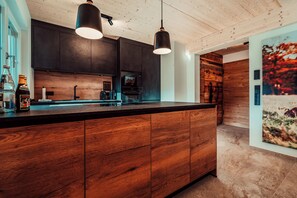 A modern kitchen with wooden cabinetry, a central island, pendant lighting, and a built-in oven. - Forestum - Black Forest Luxury Apartments - Apartment Rothirsch with sauna (Sankt Blasien)