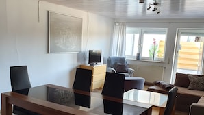 A modern living room with a dining area, a sofa, a TV, and a window with curtains. - Holiday Home 'Island Pferdehof Arrisholt Solskin' with Private Terrace, Shared Garden & Wi-Fi (Kißlegg)