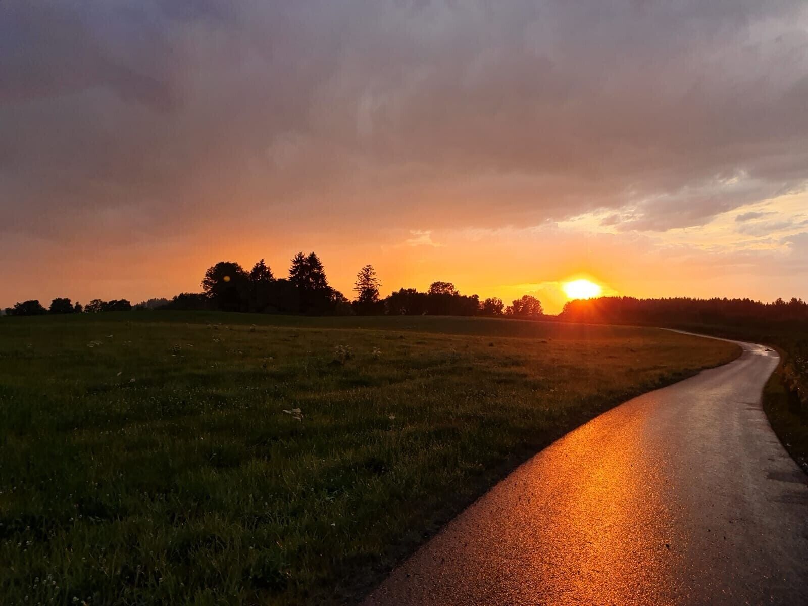 Een landweg die door een veld kronkelen, met een zonsondergang in de verte.