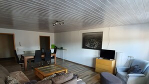 A modern living room with a sectional sofa, a coffee table, a TV stand, and a dining area with chairs and a table. - Holiday Home 'Island Pferdehof Arrisholt Solskin' with Private Terrace, Shared Garden & Wi-Fi (Kißlegg)