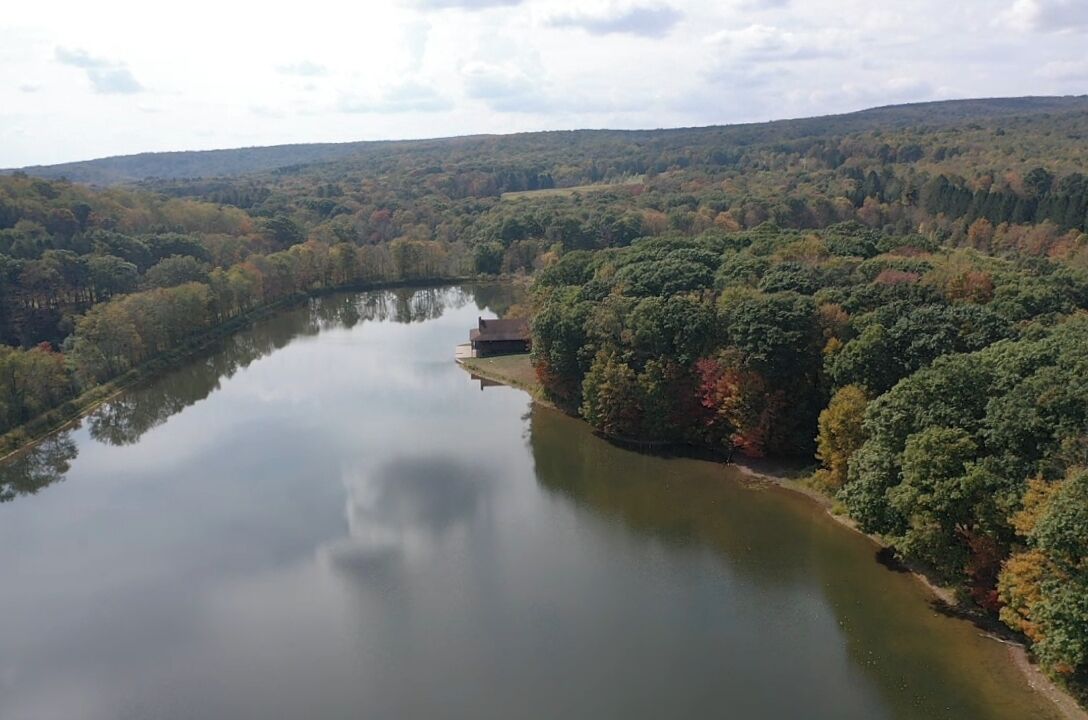Un lac paisible, entouré d’une forêt dense, un petit bâtiment situé près du bord de l’eau et, au loin, un paysage vallonné.
