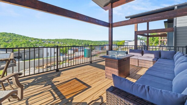 A covered outdoor deck with a wooden floor, a sofa, a table, and a grill. - Modern Table Rock Lake Retreat | Swim Dock + Pool (Reeds Spring)