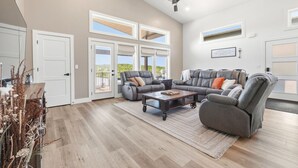 A spacious living room with a sectional sofa, a coffee table, and a ceiling fan. - Modern Table Rock Lake Retreat | Swim Dock + Pool (Reeds Spring)
