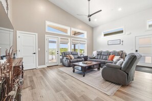 A spacious living room with a sectional sofa, a coffee table, and a ceiling fan. - Modern Table Rock Lake Retreat | Swim Dock + Pool (Reeds Spring)