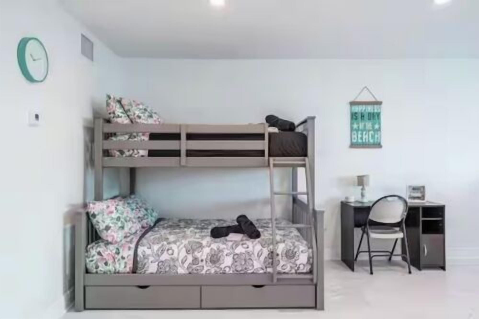 A bunk bed with a desk and chair, a clock, and a wall sign.