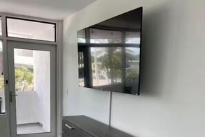 A modern room with a large flat-screen TV mounted on the wall, a sliding glass door leading to an outdoor area, and a small cabinet below the TV. - The Purple Pelican~Beachfront w/ Ocean Balcony~#5 (Fort Lauderdale)