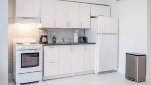 Una cucina moderna con mobili bianchi, un fornello, un frigorifero e un cestino.