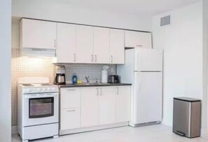 A modern kitchen with white cabinets, a stove, a refrigerator, and a trash bin. - The Purple Pelican~Beachfront w/ Ocean Balcony~#5 (Fort Lauderdale)