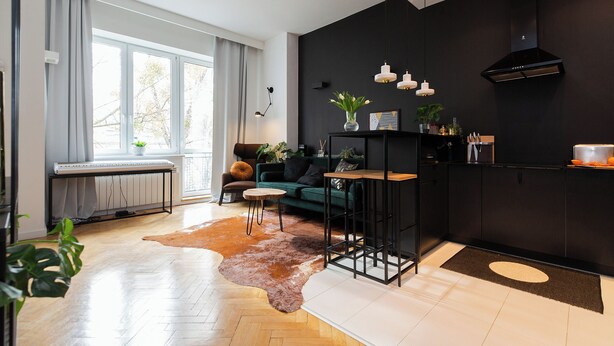 A modern living room with a herringbone floor, a green sofa, a coffee table, and a black kitchen area with pendant lights. - ShortStayPoland Orla B61 (Warsaw)