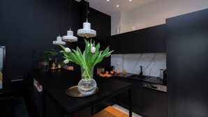 A modern kitchen with black cabinetry, a marble backsplash, and a central island with a vase of flowers. - ShortStayPoland Orla B61 (Warsaw)